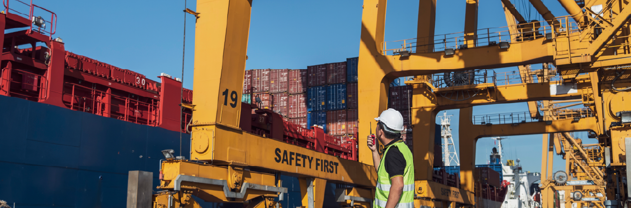 worker working with radio transceiver for controlling crane to loading container box to container ship in port shipping containers. logistics, sea transportation and logistics business concept